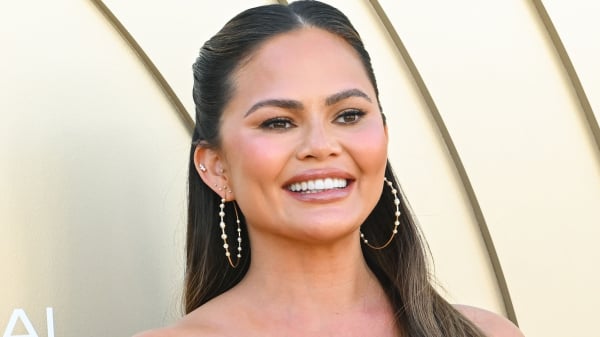 Chrissy Teigen smiling against a gold background